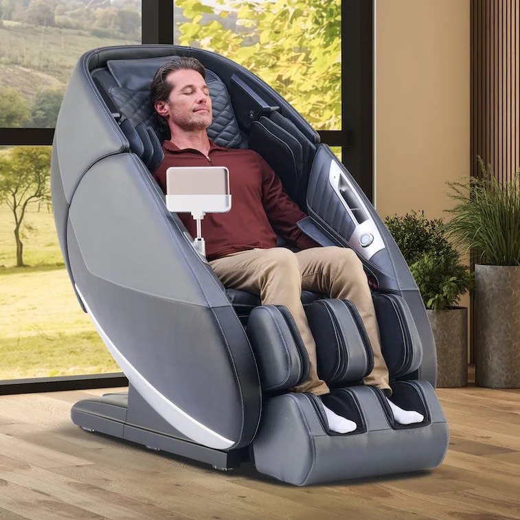 A man reclining in a Relax The Back zero-gravity massage chair beside floor-to-ceiling windows