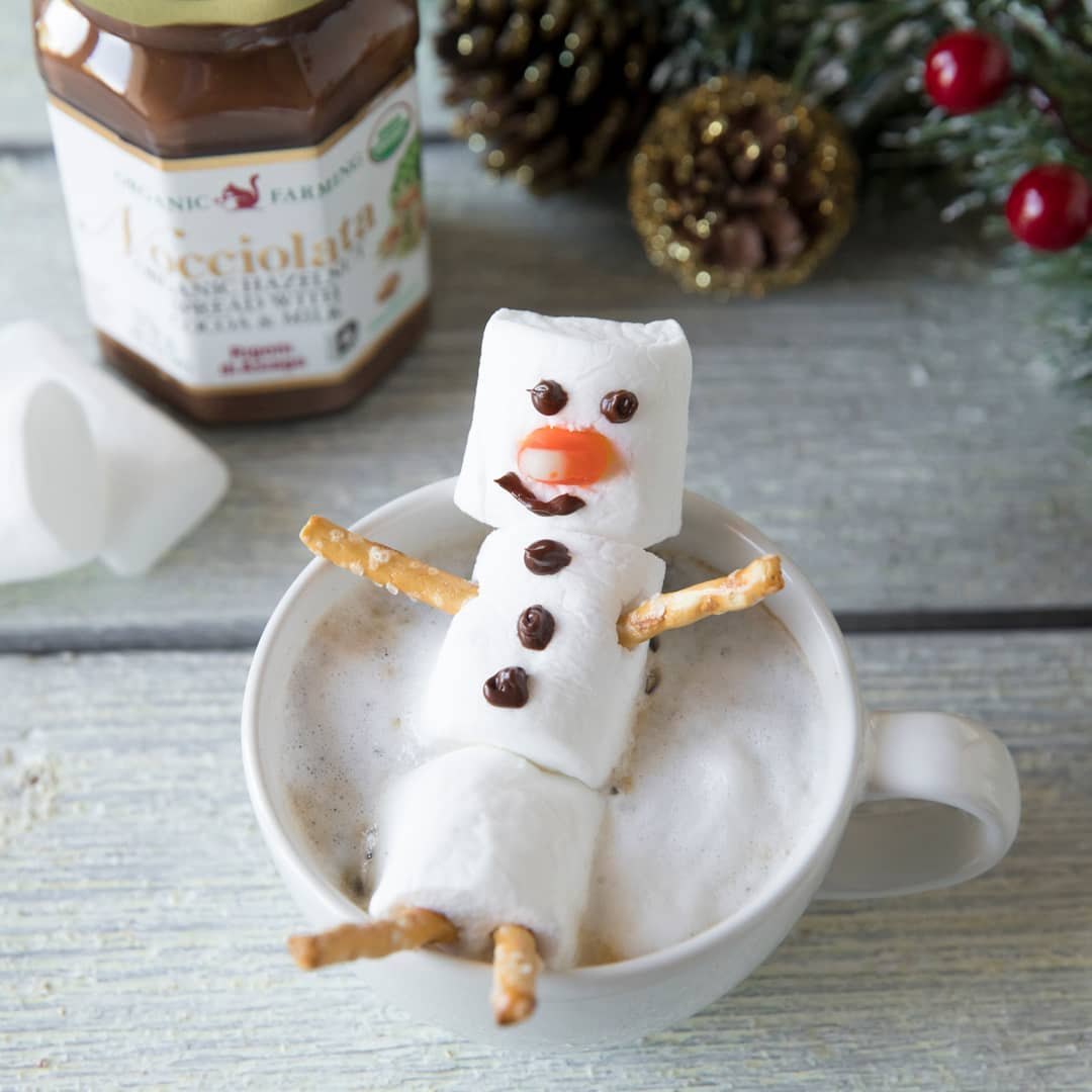 A marshmallow snowman in a mug of hot cocoa decorated with Rigoni di Asiago Nocciolata hazelnut spread