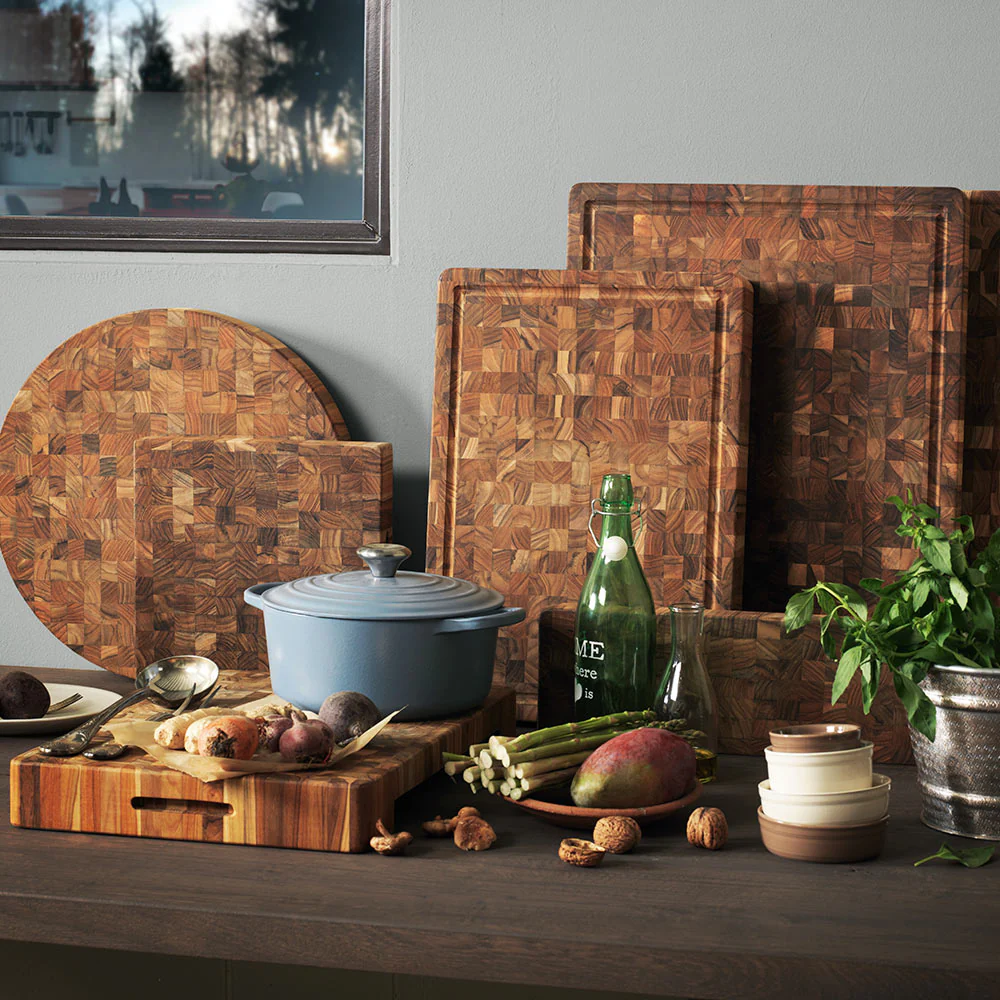 Teakhaus end-grain teak cutting and carving boards styled on a kitchen counter with produce and cookware